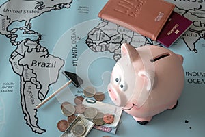 High-angle view of a piggybank, money, passport over the world map - travel savings concept