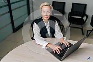 High-angle view portrait of elegance gray-haired middle-aged business woman using laptop computer sitting at workplace