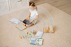 High-angle view of primary little child girl doing homework using laptop computer for distance education online sitting