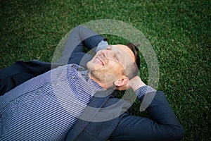 Happy Young businessman in a suit lying on the green grass and relaxing in park.