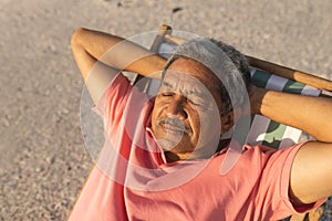 High angle view of retired senior biracial man sleeping with hands behind head on chair at beach