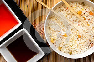 High angle view of sauces and a bowl of cooked rice with vegetables on the table