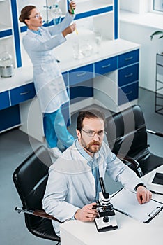 high angle view of scientist in white coat at workplace with microscope