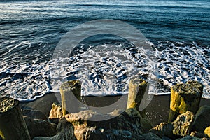 High-angle view of the sea waves touching the sandy shore with stones and dorics under the sunlight