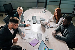 High-angle view of serious businessman signing trust partnership contract at group meeting with multiethnic partners at