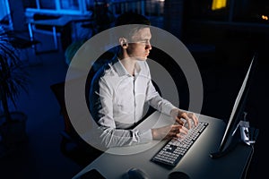 High-angle view of serious businessman working on computer in company office sitting at desk at night in dark room with