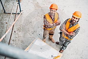 high angle view of smiling builders with blueprint standing at construction site and looking