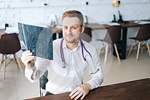 High-angle view of smiling male doctor in white uniform examining brain computerized tomography scan sitting at desk in