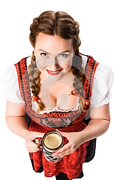high angle view of smiling oktoberfest waitress in traditional bavarian dress holding mug of dark beer