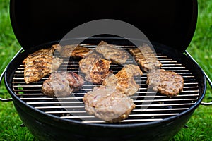 High angle view of succulent steaks and burgers cooking on a barbecue over the hot coals on a green lawn outdoors.