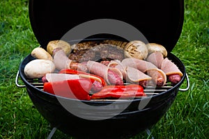 High angle view of succulent steaks,burgers, sausages and vegetables cooking on a barbecue over the hot coals on a green lawn