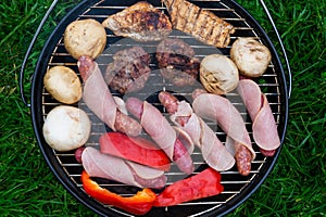 High angle view, succulent steaks,burgers,sausages and vegetables cooking on a barbecue over the hot coals on a green lawn outd