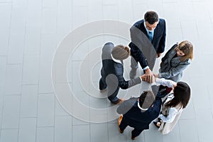 High angle view of a team of united coworkers standing with their hands together in a huddle in the modern office