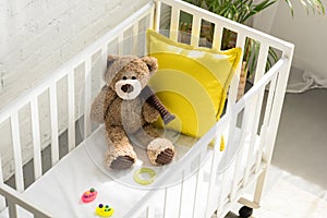 high angle view of teddy bear, other toys and yellow pillow in baby crib