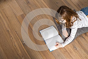 High angle view of teenage girl reading book on floor at home