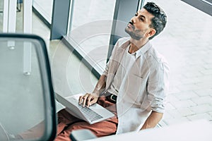 high angle view of thoughtful businessman in casual clothes sitting on floor with laptop and looking up.