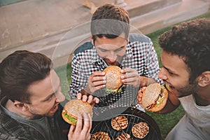 High angle view of three young men eating fresh hamburgers