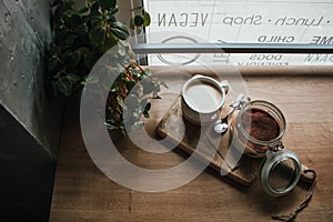 High angle view of tiramisu in glass cup with coffee cappuccino. In vegsn shop, local cozy cafe. Wooden background, candid style.