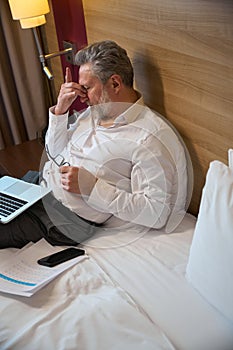 High angle view tired adult caucasian businessman during work on bed