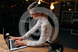 High-angle view of tired young businessman remote working overtime, learning online late at night in dark room using