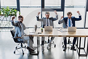 high angle view of triumphing young businessmen working with laptops