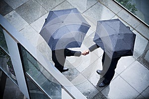 High angle view of two businessmen holding umbrellas and shaking hands in the rain