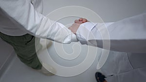 High angle view unrecognizable boy and pediatrician taking hands walking away in slow motion. Caucasian child and woman