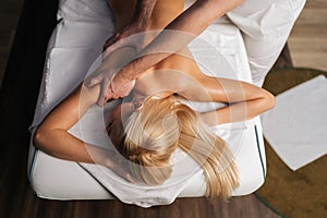 High-angle view of unrecognizable male masseur doing back and shoulder massage to blonde female with beautiful skin