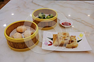 High angle view of a variety of traditional dim sum dishes on dining table in restaurant. Dumplings in bamboo steamer baskets, and