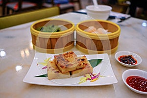 High angle view of a variety of traditional dim sum dishes on dining table in restaurant. Dumplings in bamboo steamer baskets, and