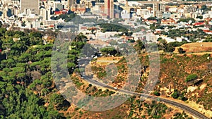 High angle view of vehicles driving on road in nature. Tilt up reveal of buildings in large city. Cape Town, South
