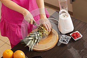 Woman cutting pineapple with a kitchen knife