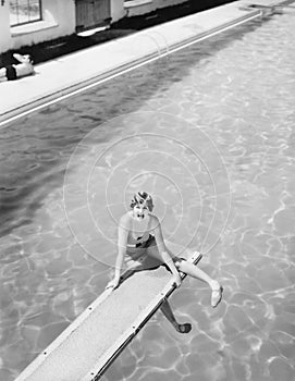 High angle view of a woman sitting on a diving board and looking feared