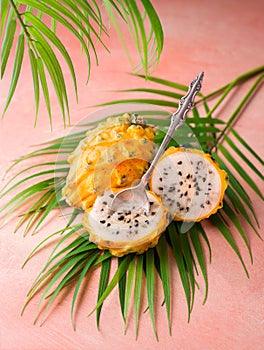 High angle view of yellow Pitaya cut in half on palm leaves with a spoon