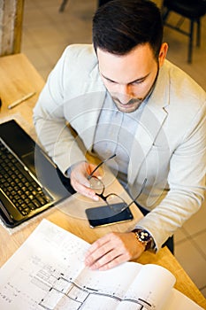 High angle view of young architect looking over building plans in modern office