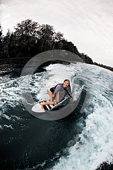 High angle view of a young smiling woman riding on surf board and look at camera