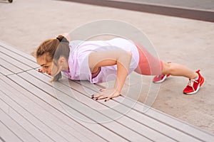 High-angle view of young sportive woman wearing activewear training doing push ups using street bench in city park at