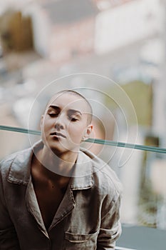 High angle view of young unhappy woman with cancer sitting in a window.