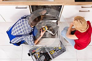 Woman Looking At Repairman Repairing Dishwasher