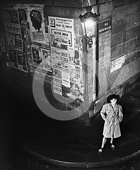 High angle view of a young woman waiting next to a lantern on a dark street corner