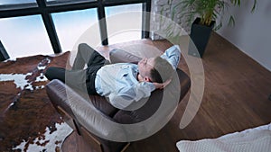 High angle view zoom in to confident relaxed businessman placing hands behind head sitting in armchair. Caucasian young