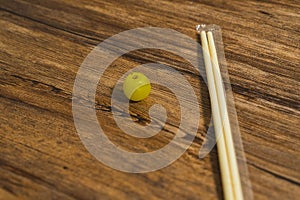 High angle of a yellow grape and a pair of chopsticks placed on a wooden table.