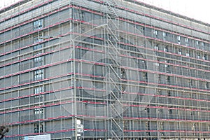 High apartment house in construction, rough building covered  by  scaffolding and protective net. Lateral view presenting two sid