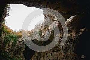 High arches of a huge stone cave with round holes at the top, a tourist road with a fence inside the cave.