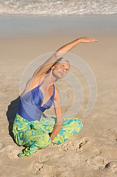 High bangle view of woman exercising while sitting on sand