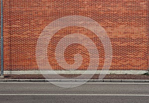 High brick wall with a porphyry sidewalk and an asphalt street in front. Urban background