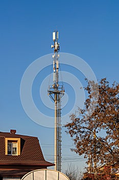 A high cell tower with antennas on top, in a city near residential buildings, against a clear sky