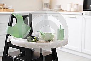 High chair with broccoli and set of baby tableware on tray indoors