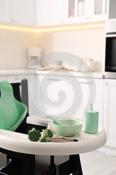 High chair with broccoli and set of baby tableware on tray indoors