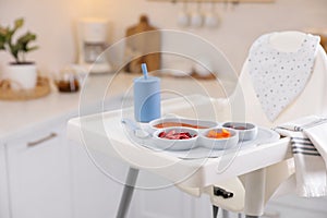 High chair with food in baby tableware on tray indoors